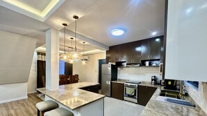 Una cocina moderna con una isla central, armarios oscuros y un comedor con sillas de madera.