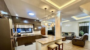 Una cocina moderna con armarios oscuros, una isla de mármol e iluminación colgante.