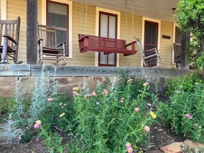 Relax on the porch with a swing and two comfortable chairs, surrounded by lush greenery.
