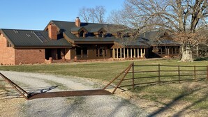A large, two-story brick house with a metal roof, a covered porch, and a fenced yard.