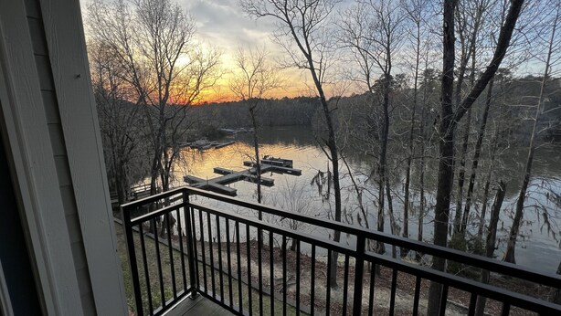 A balcony with a view of a lake and dock, surrounded by trees. - Lake Side Condo Getaway (Santee)
