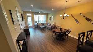 A spacious living room with a dark wood floor, a dining area with a wooden table and chairs, and a ceiling fan. - Lake Side Condo Getaway (Santee)