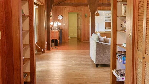 A wooden hallway with a chandelier, a sofa, and shelves.