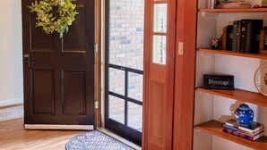 A wooden door with a wreath, a bookshelf with books and decorative items, and a patterned mat at the entrance.
