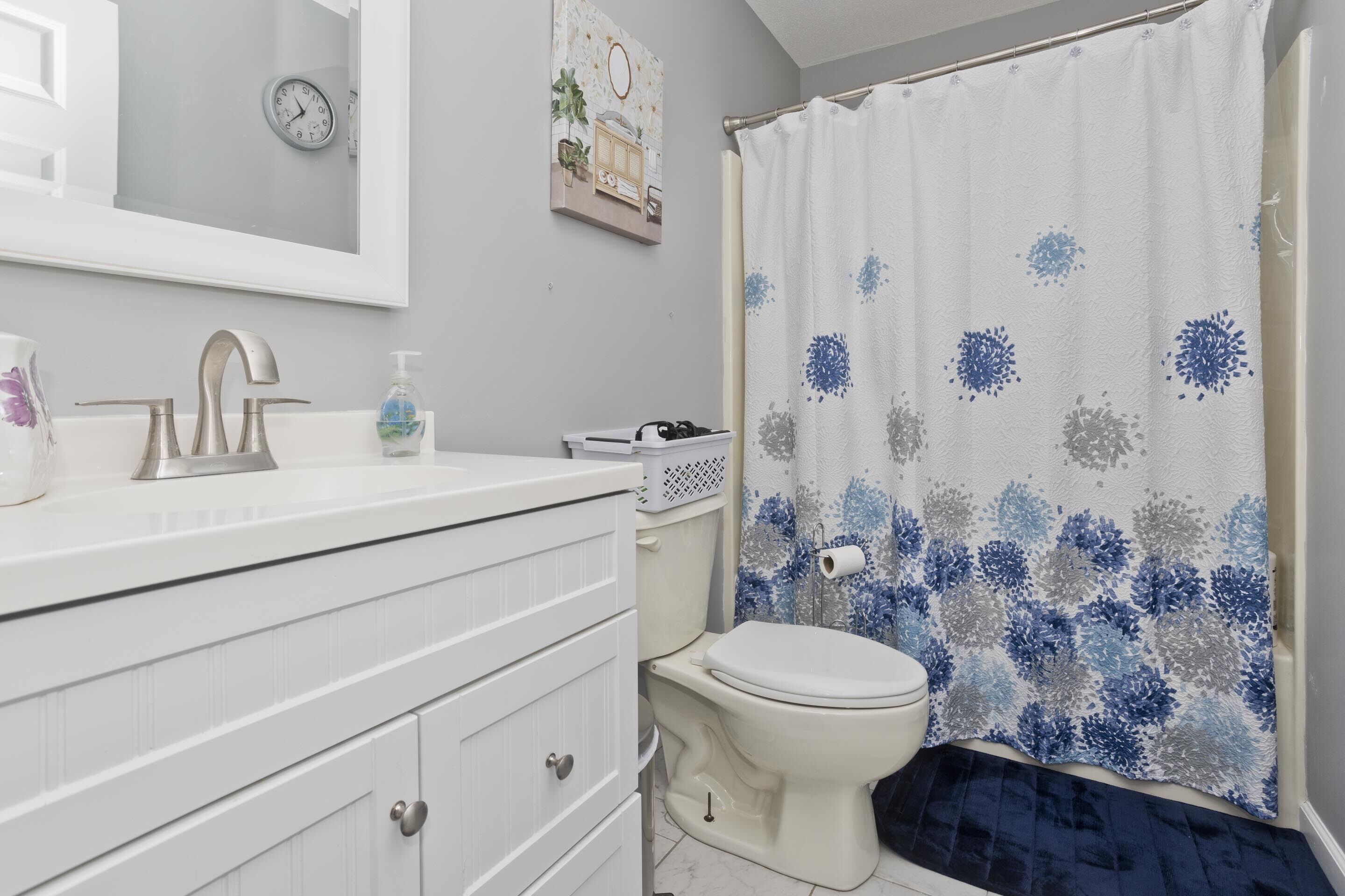 A bathroom with a white sink, a mirror, a toilet, and a shower curtain with a blue floral pattern.
