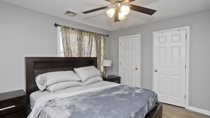 Een slaapkamer met een bed, nachtkastjes, een plafondventilator en twee deuren.