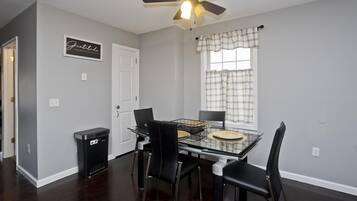 A dining area with a glass table, black chairs, a ceiling fan, and a window with plaid curtains.