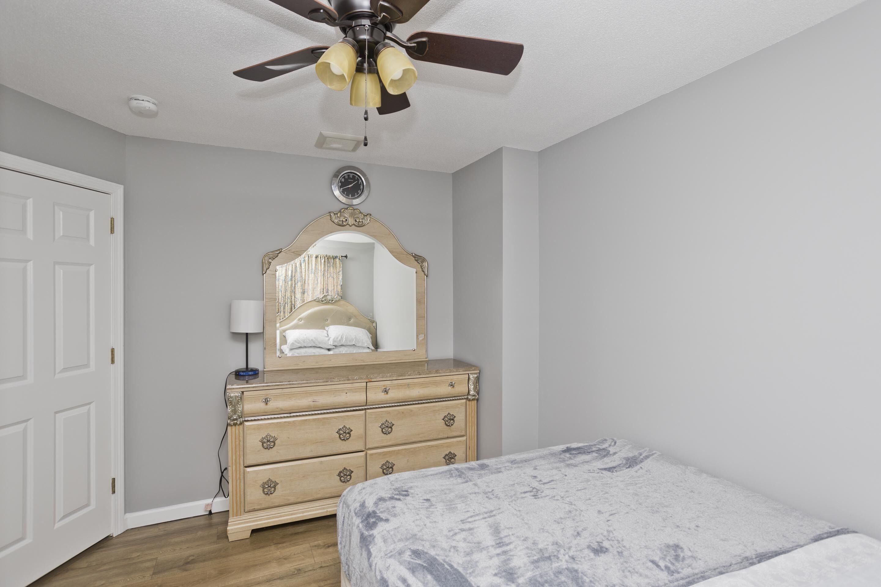 Une chambre à coucher comprenant un lit, une commode, un ventilateur de plafond et une horloge murale.