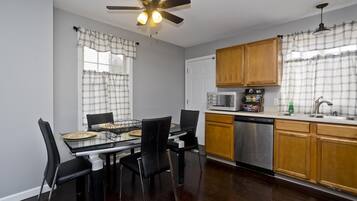 A kitchen with a dining table, chairs, a ceiling fan, wooden cabinets, a microwave, and a dishwasher.