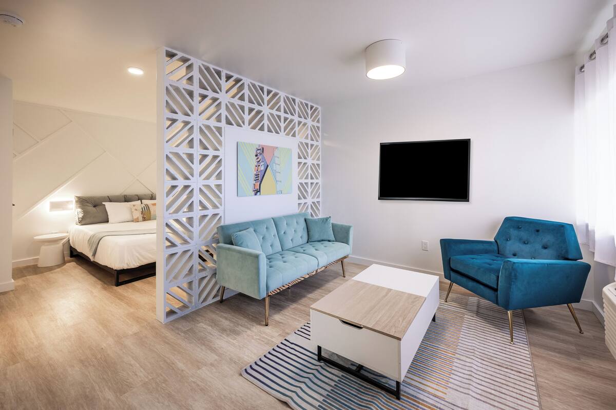 A modern bedroom with a bed, a blue sofa, a white coffee table, and a TV.