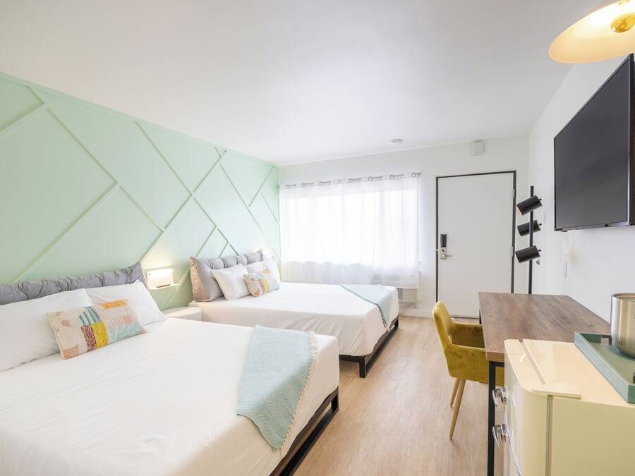 A hotel room with two beds, a dining table, a TV, and a kitchenette.