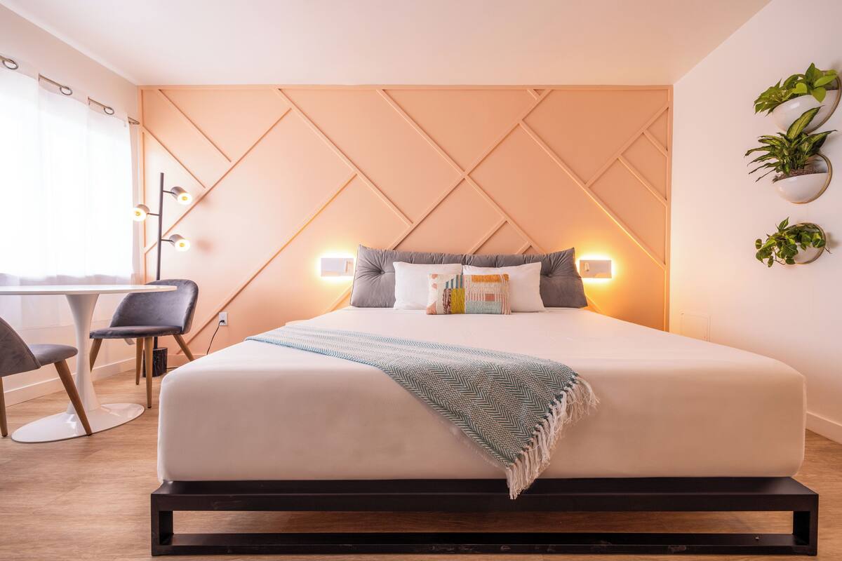 A modern hotel room with a bed, bedside table, chair, and wall-mounted plants.