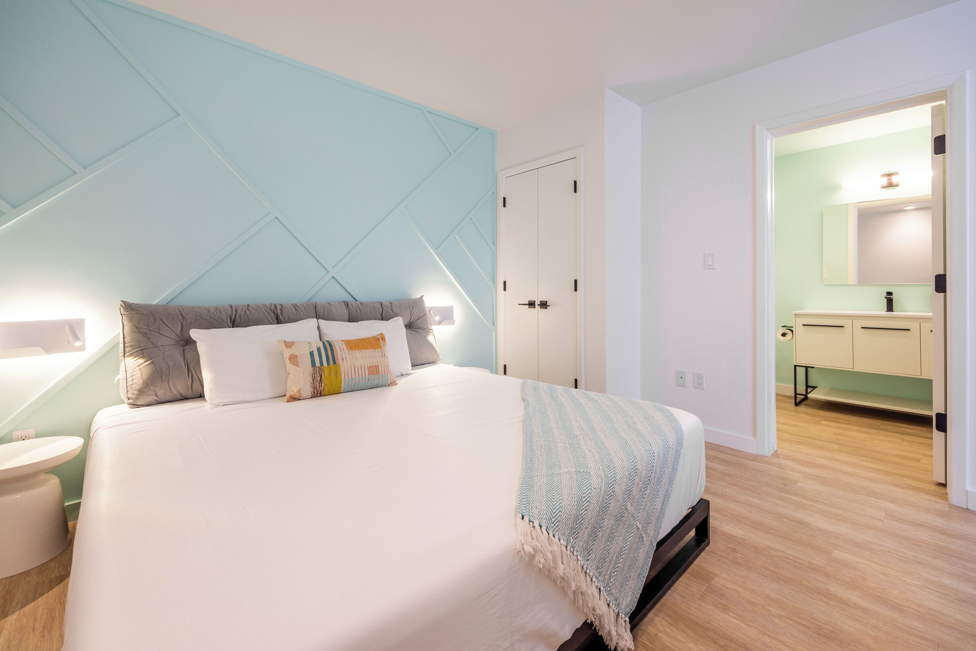 Un dormitorio moderno con una cama grande, una mesita de noche, un armario y un baño visible a través de una puerta abierta.