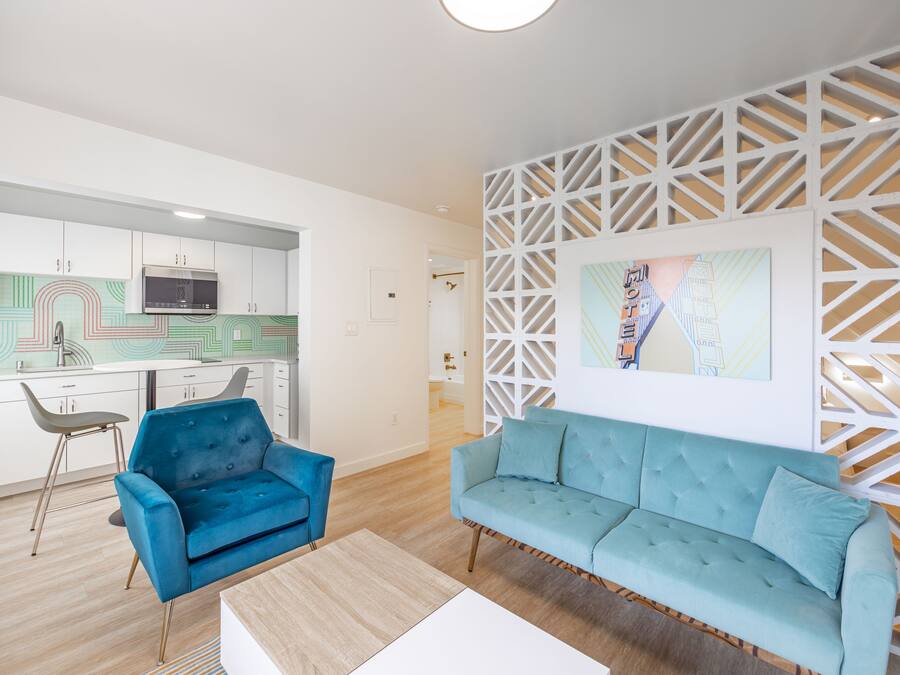 A modern living room with a blue sofa and armchair, a wooden coffee table, and a kitchen in the background.