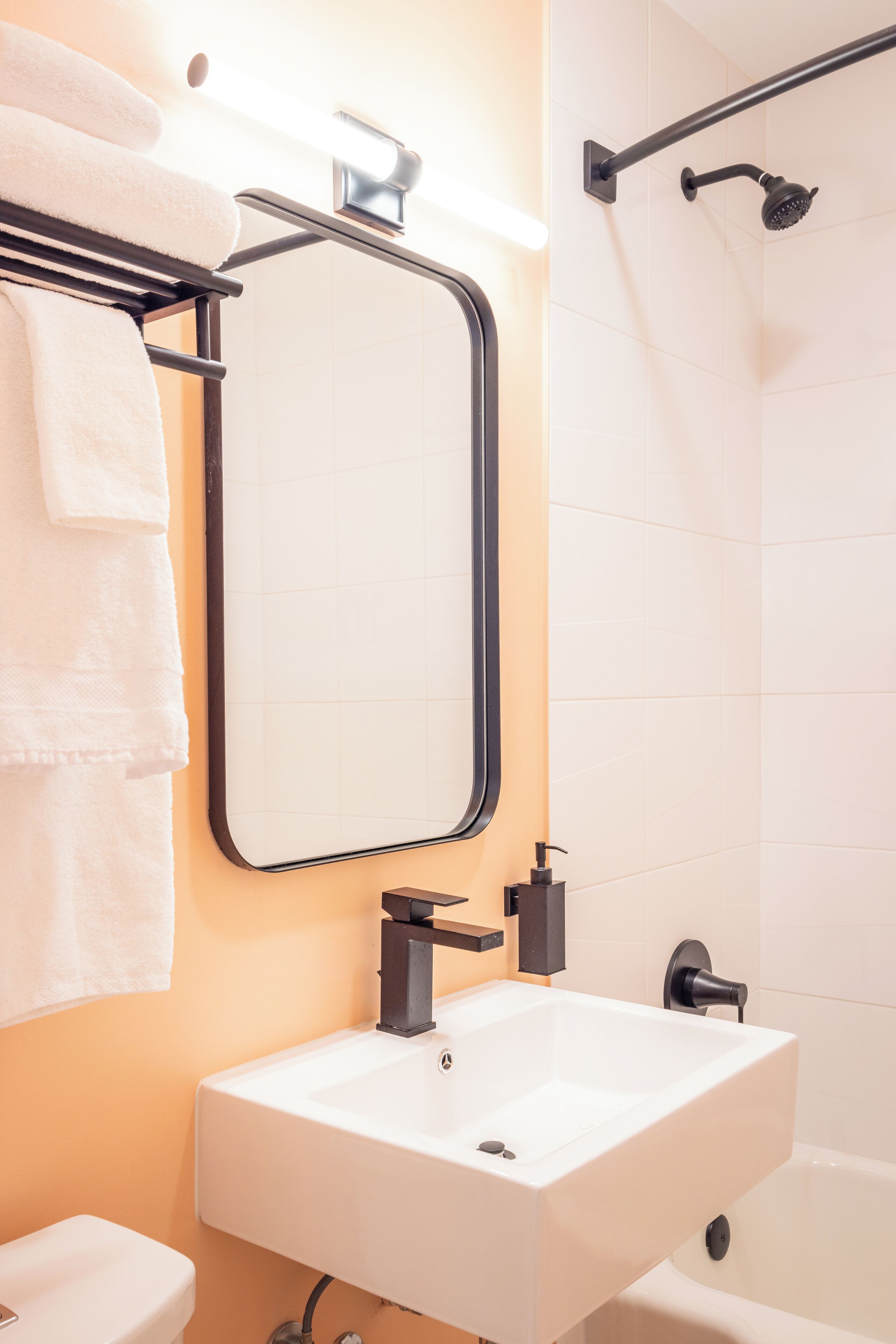 A bathroom with a white sink, a mirror, a towel rack, and a shower area.