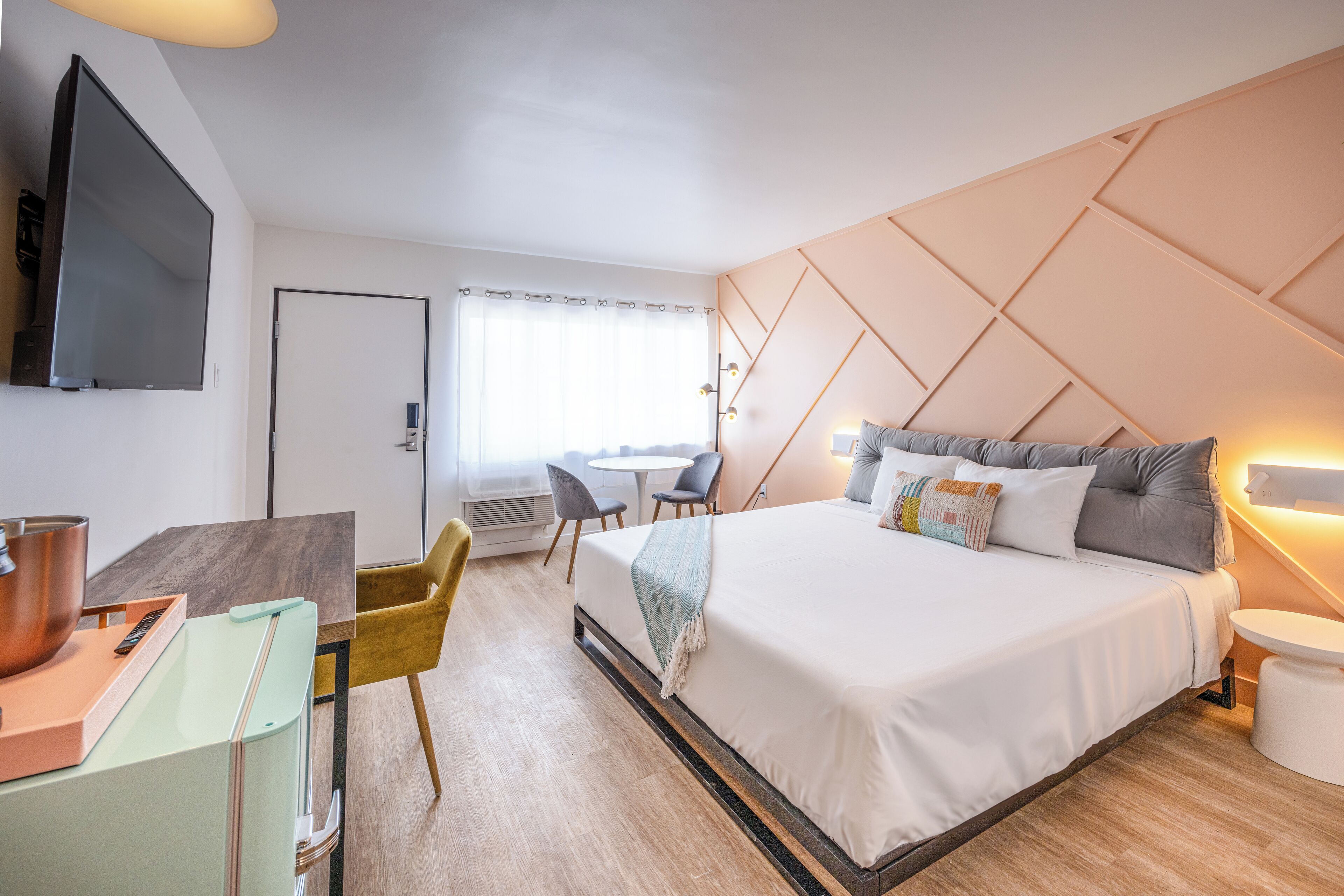 A modern hotel room with a large bed, a desk with a laptop, a television, and a dining area with chairs.