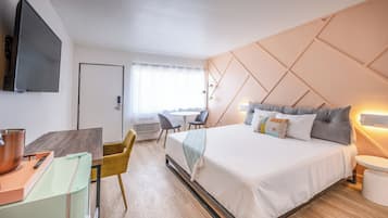 A modern hotel room with a large bed, a desk with a laptop, a television, and a dining area with chairs.
