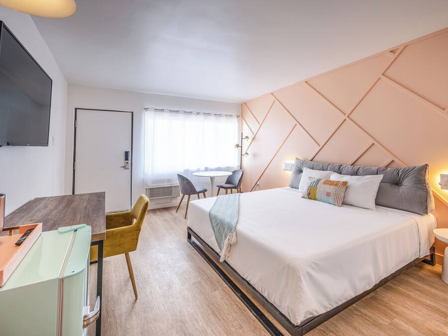 A modern hotel room with a large bed, a desk with a laptop, a television, and a dining area with chairs.