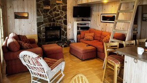 A cozy cabin interior with a stone fireplace, wooden walls, a loft bed, and a dining area. - Lake Willoughby Direct Waterfront (Westmore)