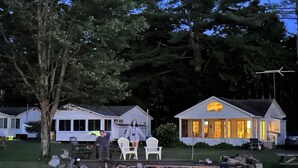 A row of cabins with a wooden deck and chairs, surrounded by trees. - Lake Willoughby Direct Waterfront (Westmore)