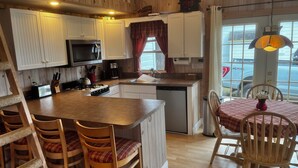 A cozy kitchen with wooden cabinets, a central island, and a dining area with a table and chairs. - Lake Willoughby Direct Waterfront (Westmore)