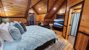 Een knus slaapkamer in een houten hut met een bed, een televisie en een raam met uitzicht op een prachtig landschap.