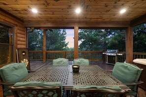 Une terrasse extérieure couverte, avec une table et des chaises en bois, un barbecue et une vue sur les arbres.