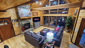 Een gezellig cabin interieur met een stenen openhaard, leren bank en een groot televisiescherm waarop 'NETFLIX' wordt weergegeven.