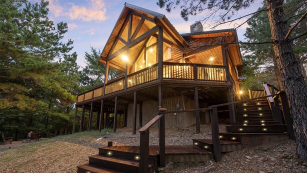 Een houten chalet met een balkon en een trap die erheen leidt, omringd door bomen.