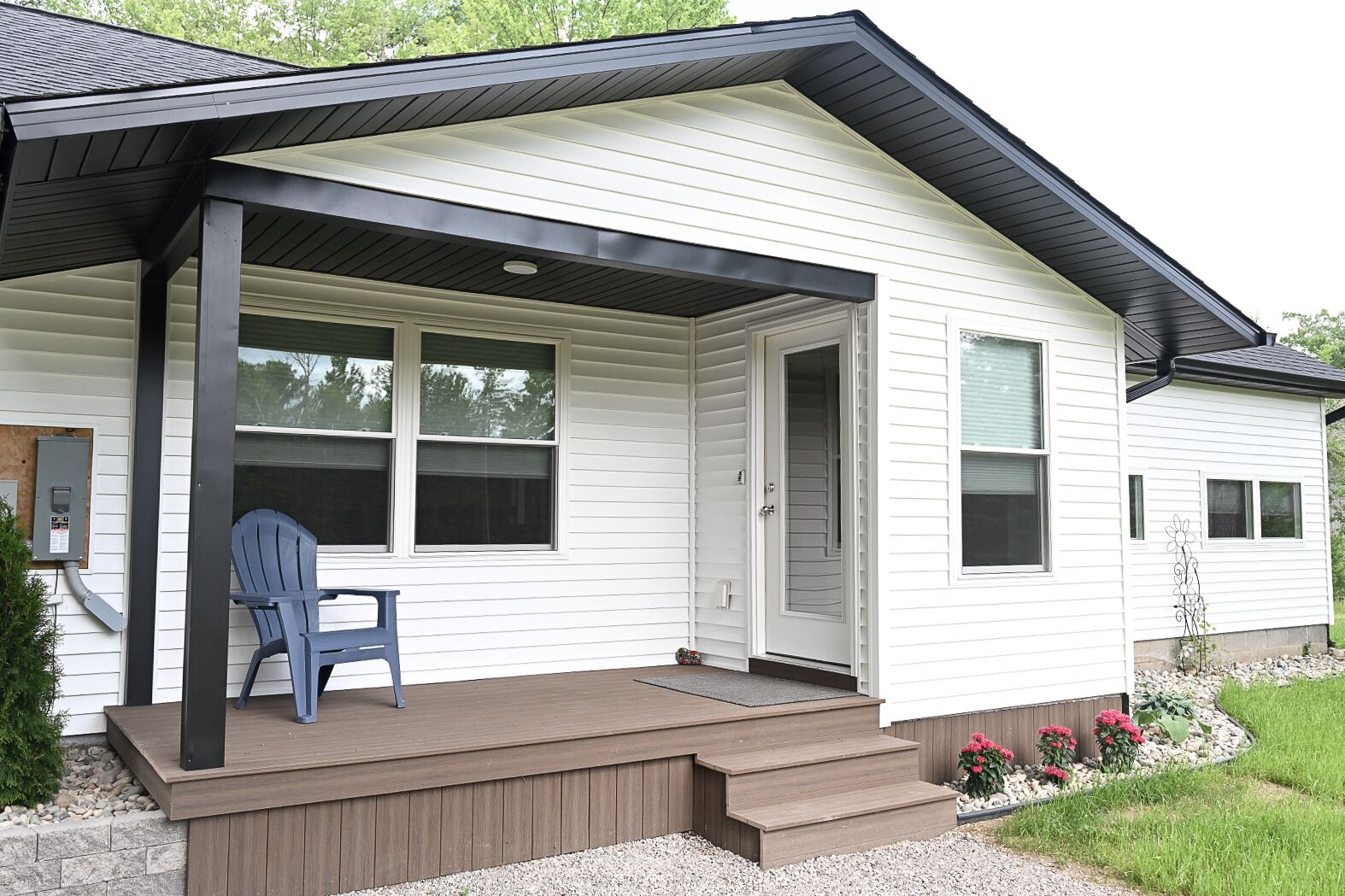 A single-story house with a covered porch, a front door, and a small outdoor seating area with a chair.