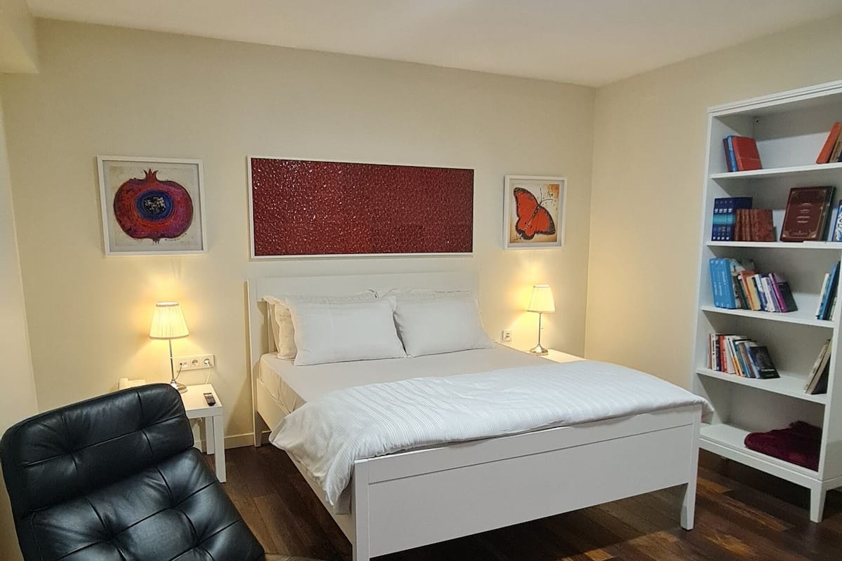 A bedroom with a bed, a black leather chair, a bookshelf, and a patterned rug.