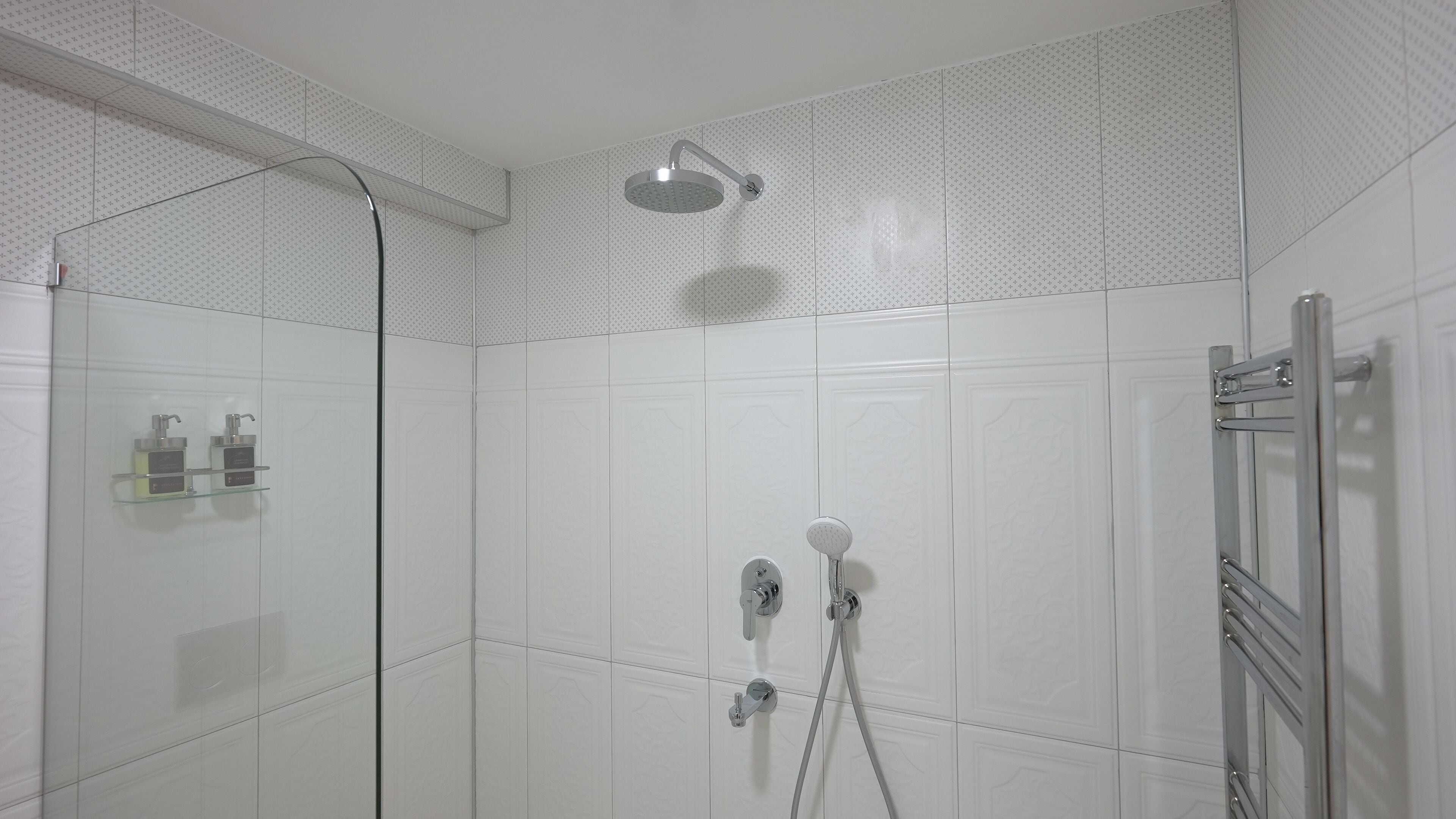 Un área de ducha moderna con mampara de vidrio, cabezal de ducha de mano y grifo empotrado en la pared.