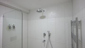 Un área de ducha moderna con mampara de vidrio, cabezal de ducha de mano y grifo empotrado en la pared.