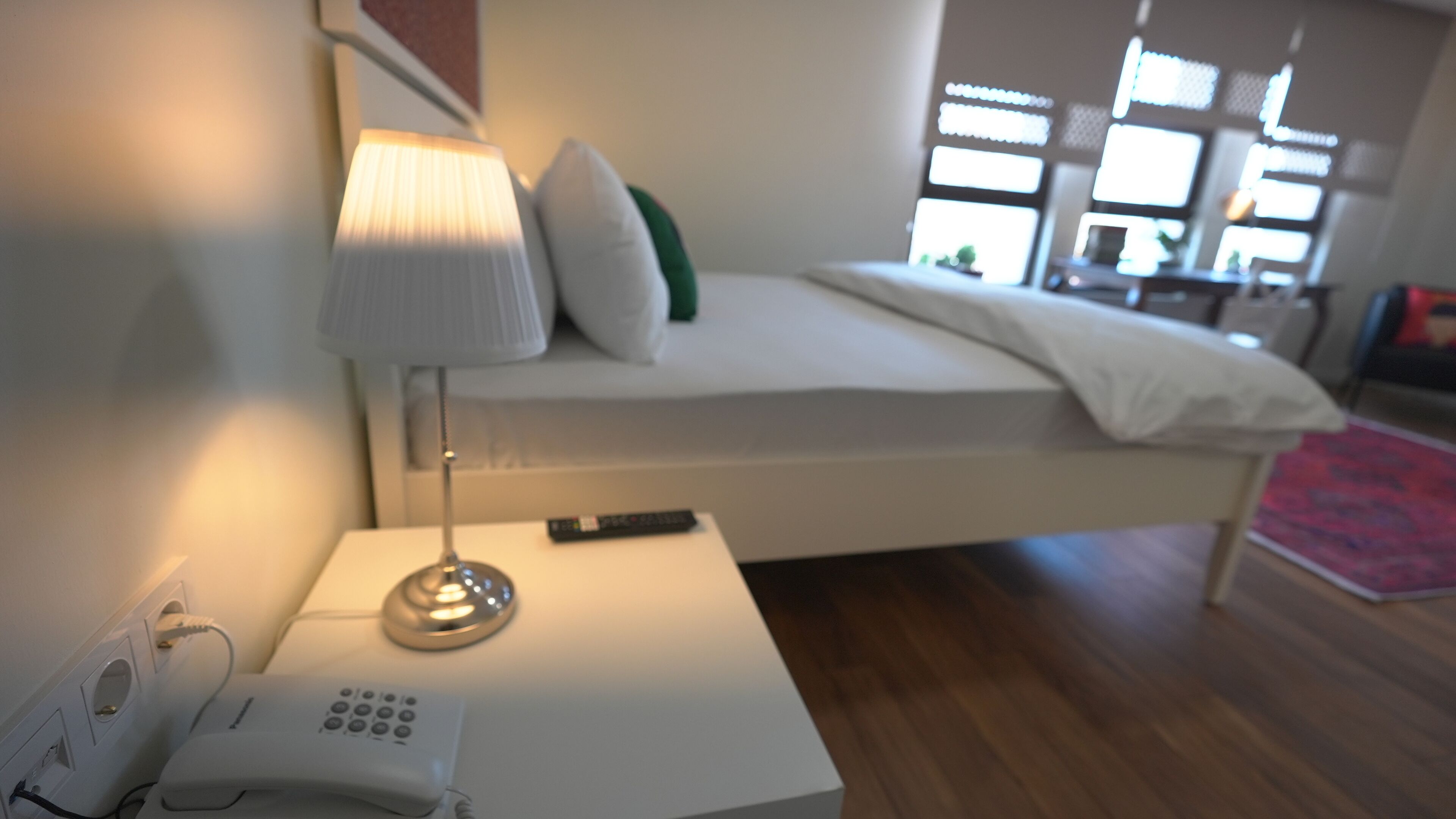 A modern bedroom with a bed, bedside lamp, and a phone on a nightstand.