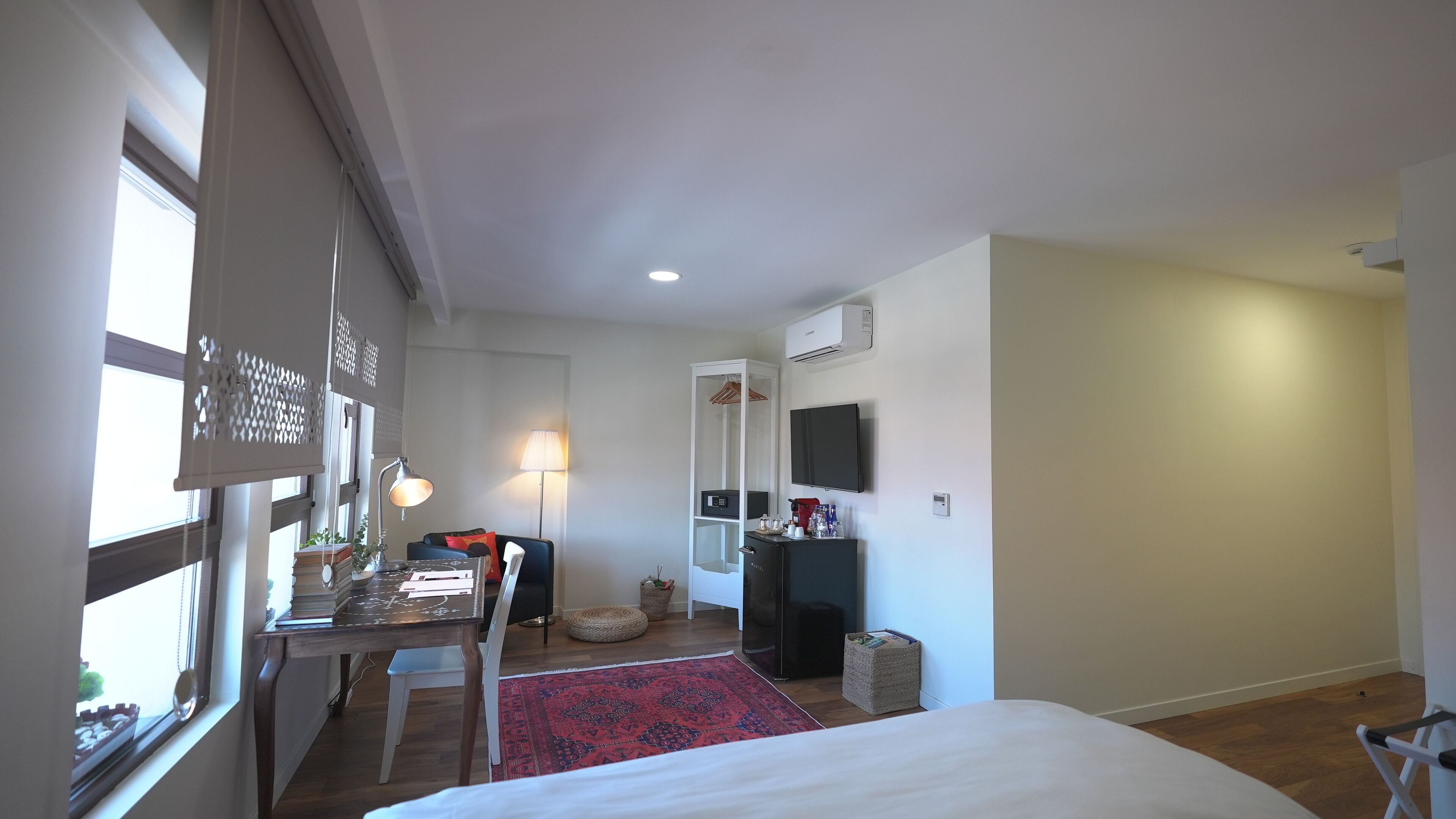 A bedroom with a bed, a desk with a lamp, a TV, and a wardrobe.