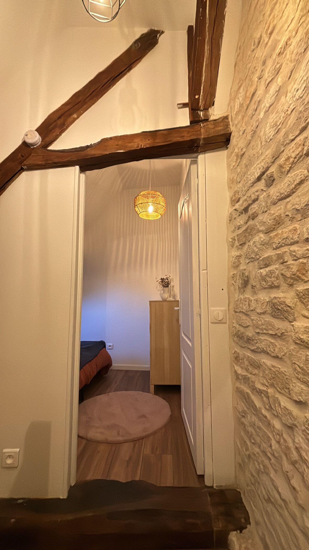 Ein schmaler Korridor mit Holzbalkendecke, einer Steinsäule rechts und einer hängenden Leuchte.