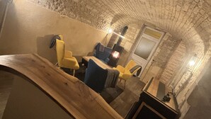 A stone-walled room with a wooden bench, a table, and yellow chairs. - La Maison de Pierre (Chablis)
