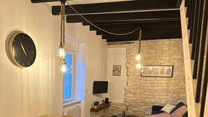 A modern living room with a stone floor, a wooden dining table, a sofa, and a staircase. - La Maison de Pierre (Chablis)