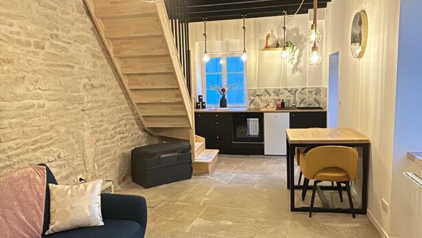 A cozy living room with a blue sofa, a coffee table, and a staircase leading to a kitchen area. - La Maison de Pierre (Chablis)