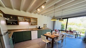 A modern kitchen with green cabinets, a wooden dining table, and a large window overlooking greenery. - Villa "Calypso" (SEIGNOSSE)