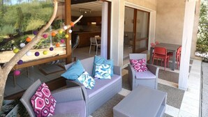 A modern outdoor seating area with a sofa and chairs, a dining table, and a decorative tree branch with colorful balls. - Villa "Calypso" (SEIGNOSSE)