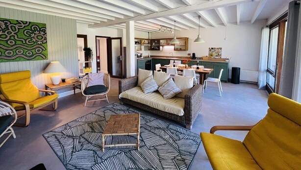 A modern living room with a sofa, chairs, and a dining table. There is a kitchen in the background with a dining area. - Villa "Calypso" (SEIGNOSSE)