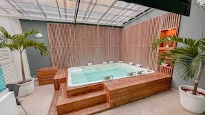 Ein moderner Poolbereich im Innenbereich mit Whirlpool, Holzstufen und Kübelpflanzen.