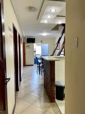 A hallway with a tiled floor, a staircase, and a counter with a trash bin.