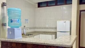 A kitchen with a granite countertop, a water dispenser, a refrigerator, and a tiled backsplash. - Prédio Atalaia  (Arraial do Cabo)