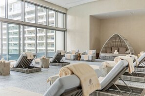 A modern spa area with reclining chairs, a hanging chair, and a view of a high-rise building. - Luxurious 5-Diamond Jr. Suite Ocean View at Garza Blanca 5-Star Resort: Cancun (Cancún)