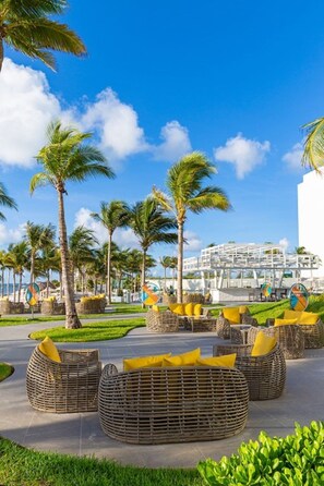 A resort area with wicker furniture, palm trees, and a modern building in the background. - Luxurious 5-Diamond Jr. Suite Ocean View at Garza Blanca 5-Star Resort: Cancun (Cancún)