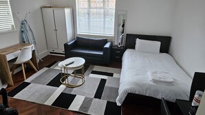 A modern hotel room with a bed, a sofa, a desk, and a wardrobe.