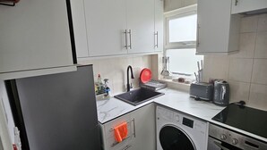 A compact kitchen with white cabinets, a black refrigerator, a washing machine, and a toaster.