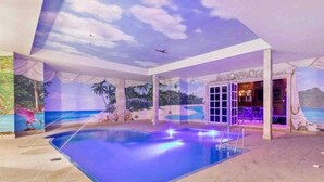 Une piscine intérieure agrémentée d’une fresque aux motifs tropicaux, d’un espace bar et d’un plafond décoré de nuages et d’avions.